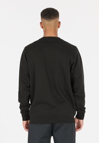 Svart crewneck sweatshirt med ribbade ärmslut och fåll, mjukt texturerat tyg och avslappnad passform, sedd bakifrån.