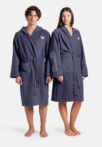 Marinblå huvar med texturerat tyg, midjebälte och logodetalj på ärmarna. Slät design som når knäna, lämplig för unisex.