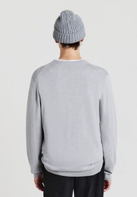 Maglione grigio chiaro con collo e polsini a coste, caratterizzato da una finitura testurizzata. Abbinato a un berretto grigio a coste coordinato.