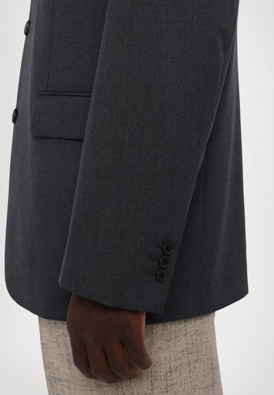 Tumes hall švarts aksessuaar, millel on tekstuurne viimistlus, ühe nööbi kinnitusega ja kolme nööbiga detailid mansetil. Kätetükk on fookuses, näidates materjali ja lõiget.