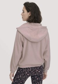 Felpa con cappuccio rosa chiaro, dotata di cappuccio, polsini elasticizzati e orlo cropped. Abbinata a leggings neri con stampa leopardata rosa.