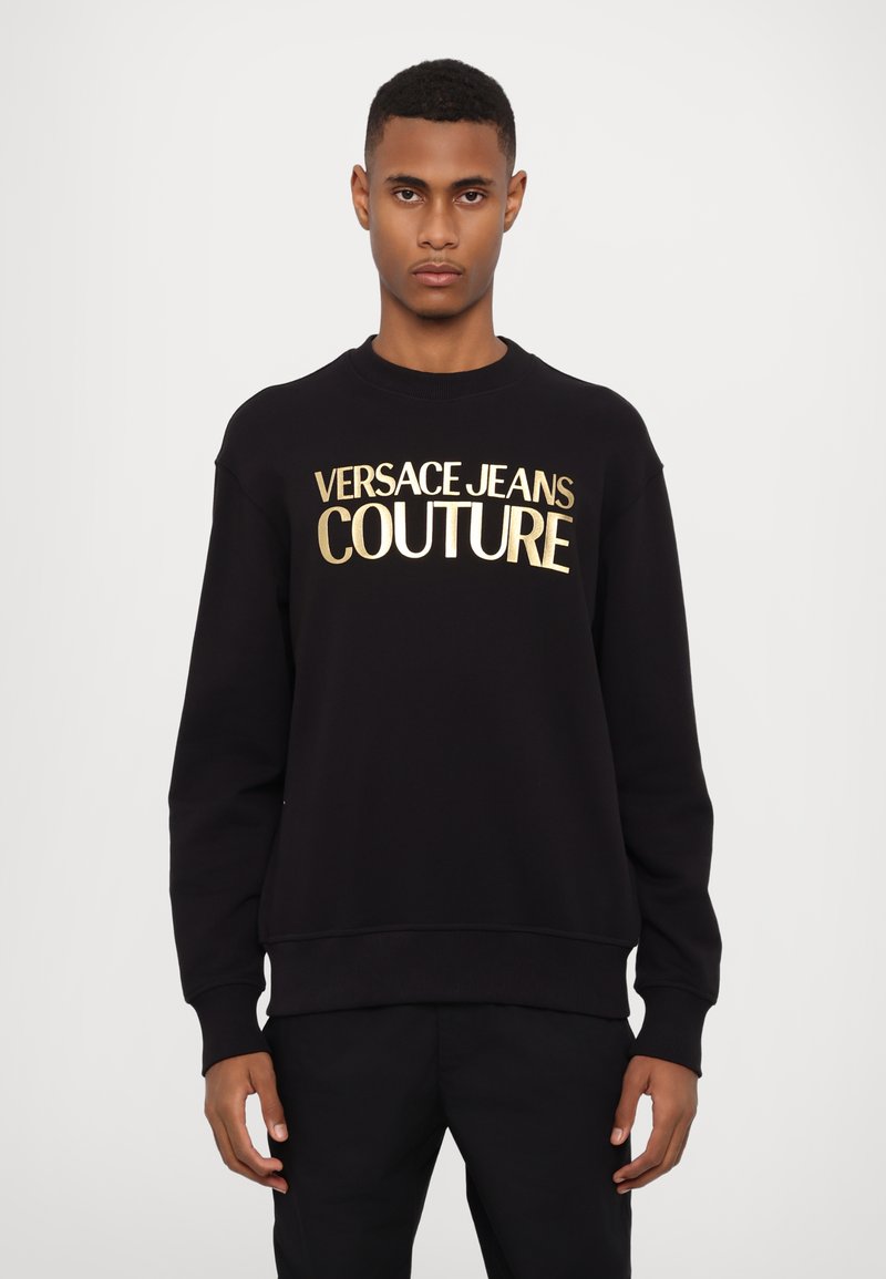 Felpa nera realizzata in tessuto dalla trama morbida, con la scritta "VERSACE JEANS COUTURE" in lettere dorate in grassetto sulla parte anteriore.