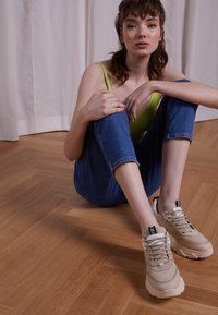 Sneaker chunky beige con parte superiore in suede testurizzato e mesh, punta rotonda, allacciatura frontale e etichette nere di accento. Indossate con jeans blu arrotolati.