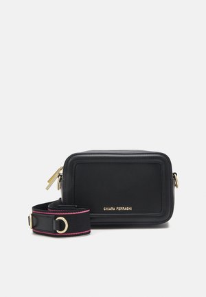 Sac bandoulière compact rectangulaire en cuir noir avec fermeture éclair dorée, sangle noire détachable aux bords roses, et logo "Chiara Ferragni" en lettres dorées.