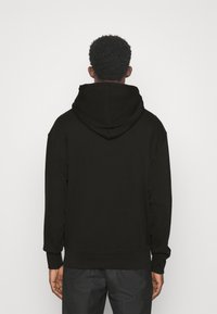 Sudadera negra con una capucha amplia, mangas largas y puños acanalados. Tejido suave y texturizado, presenta un diseño sencillo sin logotipos ni patrones.
