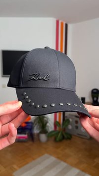 Must mustriga pesapalli nokam, millel on sile kangaspind, reljeefne logo ja dekoratiivsed naelad nokakattel. Lihtne, vormitud disain.