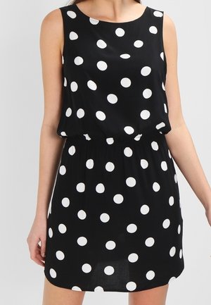 Vestido negro sin mangas con parte superior suelta y cintura ajustada, con un patrón de lunares blancos por todo el vestido.