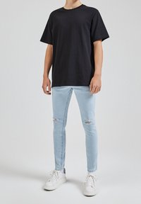 T-shirt en coton noir, col rond, manches courtes. Jean skinny bleu clair avec genoux déchirés. Baskets blanches avec semelles texturées.