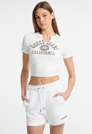 T-shirt blanc court à manches courtes avec un col rond et un logo imprimé "GUESS JEANS CALIFORNIA". Associé à un short blanc à cordon de serrage.