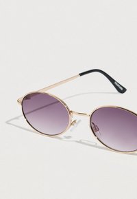 Στρογγυλά γυαλιά ηλίου με φακούς σε βαθμιαία μοβ απόχρωση, χρυστό μεταλλικό σκελετό και μαύρα βραχίωνα από ακρυλικό. Διαθέτουν μαξιλαράκια στη μύτη για άνεση.