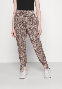 Růžové leopardí vzorované kalhoty s elastickým pasem a nařasenými manžetami. Lehká tkanina, volný střih. Nosené s bílými teniskami.