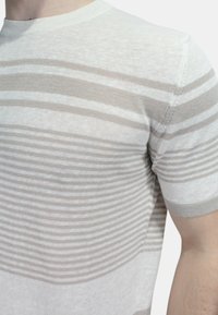 T-shirt a righe beige in maglia con scollatura a girocollo; presenta strisce di diverse larghezze alternate con una texture sottile e un tessuto morbido.