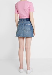 Rosa T-Shirt mit kurzen Ärmeln, kombiniert mit einem hellblauen Jeans-Minirock mit ausgefranstem Saum und zwei Gesäßtaschen, getragen mit weißen Turnschuhen.