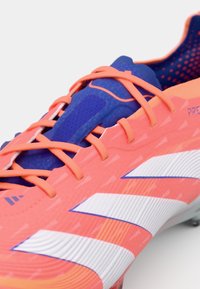 Scarpini da calcio rosa brillante con dettagli blu, dotati di tomaia testurizzata, strisce bianche prominenti e un sistema di allacciatura resistente per una calzata sicura.