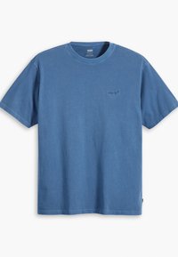 T-shirt en coton bleu avec des manches courtes, un col rond et un petit logo ton sur ton sur la poitrine. Texture douce et design décontracté.