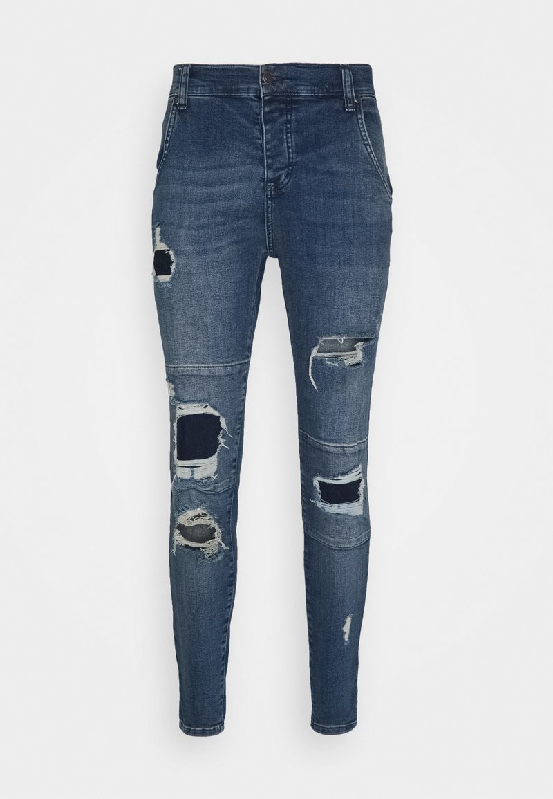 Jeans ajustados de denim azul oscuro con áreas desgastadas y diseños de parches variados. Presenta un estilo clásico de cinco bolsillos y cierre de botón.
