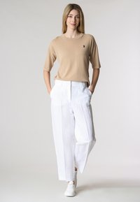 Top corto a maniche corte di colore tan con texture a costine e una piccola grafica, abbinato a pantaloni larghi in lino bianchi. Il modello indossa sneaker bianche.