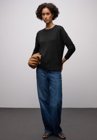 Pull noir en maille avec col rond, associé à un jean denim bleu ample. Un sac pochette marron est tenu, complété par des chaussures à imprimé léopard.