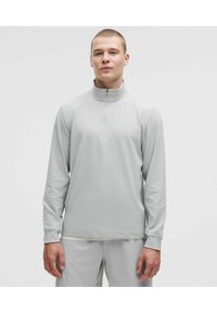 Vaaleanharmaa, pitkähihainen vetoketjupullover, jossa on sileä pinta ja vartalonmyötäinen muotoilu, sopii aktiiviseen tai rentoon käyttöön.