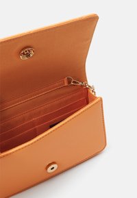 Pomarańczowy portfel ze skóry z zapięciem na złoty zatrzask, wewnętrznymi miejscami na karty oraz przegródką. Gładka faktura z minimalistycznym designem.