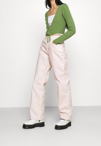 Zelený žebrovaný pletený zkrácený kardigan s vázáním, kombinovaný s růžovými kostkovanými kalhotami s širokými nohavicemi. Bílé platformové boty s černými podrážkami.