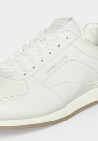 Basket en cuir blanc avec lacets blancs, semelle en caoutchouc et "Michael Kors" embossé sur le côté, montrant la vue avant supérieure et latérale.
