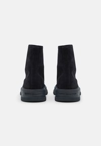 Botas de tobillo de ante negro con un acabado texturizado, que presentan una suela de goma y un logotipo grabado en la parte trasera. Diseño simple y minimalista.