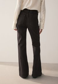 Čierne džínsové nohavice s rozšírenými nohavicami a vysokým pásom, s dvoma zadnými vreckami a čistým zakončením; nosené s ľahkou prúžkovanou košeľou.