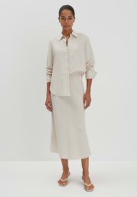 Helles beiges Hemd mit Kragen und Knöpfen, kombiniert mit einem passenden knöchellangen Rock. Glatter Stoff und entspannter Schnitt mit einem seitlichen Schlitz.