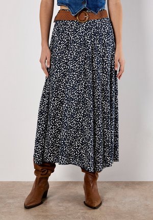 Woman wearing a navy blue and white patterned midi skirt with a wide brown belt and slouchy brown leather boots.