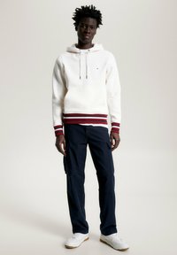 Weißer Kapuzenpulli mit roten und marineblauen gestreiften Bündchen, kombiniert mit marineblauen Cargo-Hosen und weißen Sneakern.