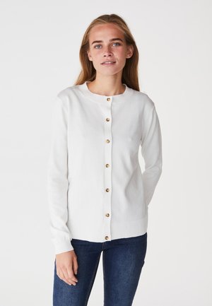 Cardigan bianco con scollo rotondo, bottoni dorati e polsini a coste. Il tessuto appare morbido con una texture liscia. Indossato sopra jeans blu.