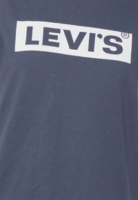 Granatowa bawełniana koszulka z dużym białym logo Levi's w prostokątnym wzorze na klatce piersiowej. Miękka tekstura i luźny krój.
