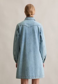 Robe en denim bleu clair, avec un col, des manches longues et une coupe décontractée. Le dos présente une couture d'empiècement et des détails de couture subtils.