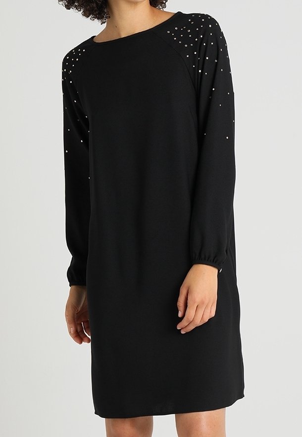 Robe noire à manches longues avec une coupe ample, dotée d'un col rond et d'épaules embellies de petits accents argentés. Matière douce.