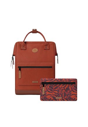 Roter Stoff-Rucksack mit doppelten Griffen und einer vorderen Reißverschlusstasche. Beinhaltet ein kleines Täschchen mit einem Blättermuster in Rottönen und Blau.