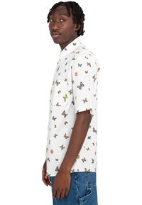 Camisa de manga corta en tela blanca, con un estampado de mariposas en varios colores. Incluye un bolsillo en el pecho y un cuello de camisa clásico.