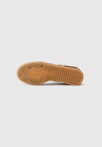 Tan rubber shoe sole with textured grip pattern. Features circular and diamond-shaped accents. Smooth edges with minimal branding visible.
