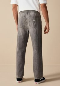 Pantaloni din denim gri cu o croială relaxată, talie elastică și două buzunare la spate. Prezintă o decolorare subtilă și o etichetă de marcă pătrată.