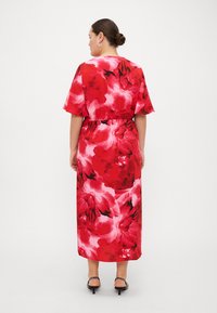 Vestido maxi vermelho com padrão floral, apresentando uma cintura elástica, mangas curtas e um padrão vibrante. As costas mostram o design fluido do vestido e o seu ajuste descontraído.