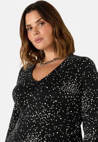 Černý dlouhý rukáv s bílými srdíčkovými vzory, se skládacím výstřihem a přiléhavým střihem pro elegantní vzhled.