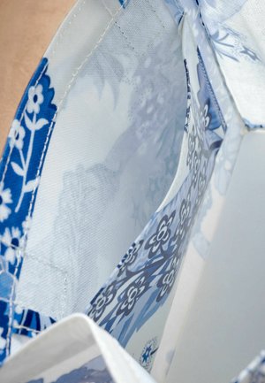 Blauw-witte stof met een bloemenpatroon en een zachte textuur, met interne zakken en een licht, luchtig ontwerp.
