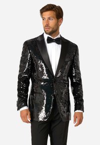 Czarna marynarka z cekinami i satynowymi klapami, z zapięciem na jeden guzik i bocznymi kieszeniami, w zestawie z białą koszulą i muchą.