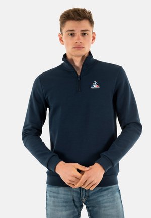 Felpa zip a collo alto di colore blu navy, con logo sul petto, maniche lunghe e design aderente. Realizzata in un tessuto morbido e liscio.