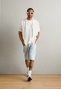Hvit kortermet skjorte over en hvit t-skjorte, sammen med lyseblå denimshorts. Tilbehøret inkluderer hvite solbriller og sporty fottøy.