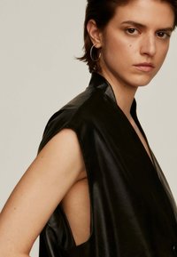 Top negro sin mangas hecho de material brillante, con grandes sisas y un cuello alto. Textura suave con un diseño minimalista.