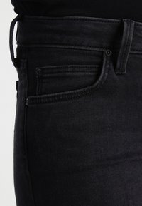 Pantalones vaqueros negros de mezclilla con una silueta ajustada, que presentan un diseño clásico de cinco bolsillos y costuras a tono. Textura suave con un acabado moderno.