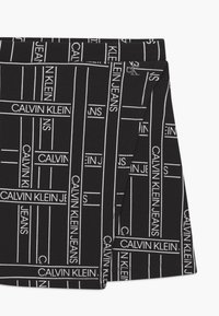 Černé šortky z měkké látky s celoplošným vzorem bílého textu, který obsahuje "CALVIN KLEIN JEANS", s moderním, priléhavým střihem.