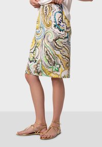 Jupe longue à motifs atteignant le genou, présentant un mélange de motifs paisley jaunes, verts, bleus et bruns sur un fond clair.