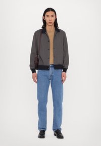 Πουκάμισο σακάκι σε σκούρο υφασμάτινο σχέδιο με γιακά, συνδυασμένο με καφέ μπλούζα και ανοιχτό μπλε τζιν. Μαύρα παπούτσια ολοκληρώνουν την εμφάνιση.